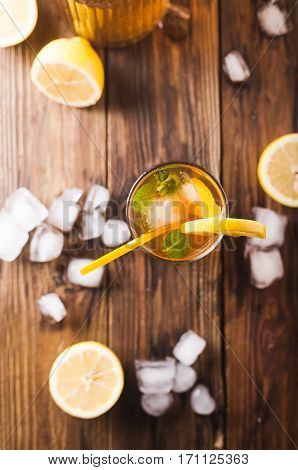 Lemon ice tea on brown wooden table with lemons around. Iced tea with lemon slices and mint on rustic background