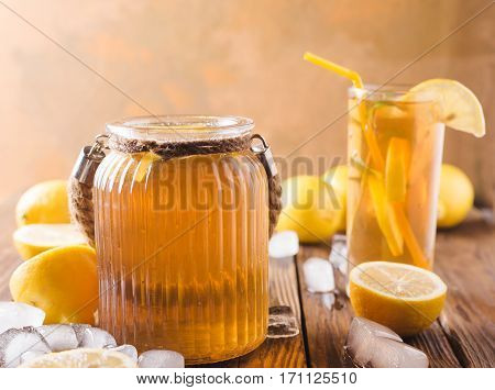 Lemon ice tea on brown wooden table with lemons around. Iced tea with lemon slices and mint on rustic background