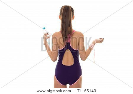 slim young brunette girl in body swimsuit with measure and bottle of water in hands from backside isolated on white