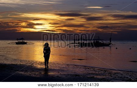 One alone woman going on coastline in colorful dramatic sunset golden hours with golden sky and boats background, one woman on sunset, golden sunset hours in tropics, amazing sunset