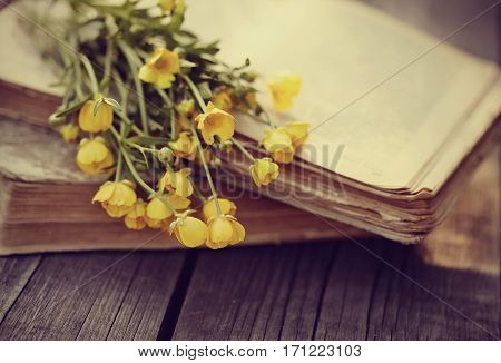 Old books and bouquet of yellow buttercups on a wooden table.
