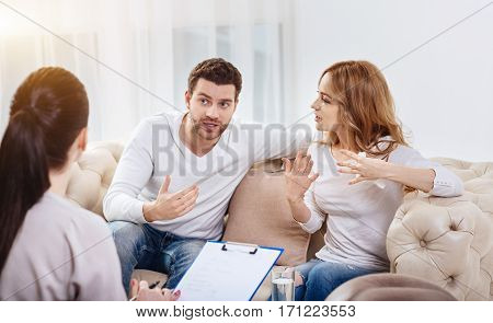Miscommunication between people. Emotional cheerless young man and woman sitting on the sofa and gesticulating while disagreeing with each other