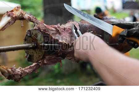 Barbecue picnic at country fair. Lamb roasted at spit. Grill, big piece of meat at rolling skewer. Street vendor, professional chef hands cooking bbq food, unrecognizable. Catering concept