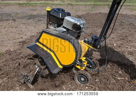 Garden tiller to work tractor cultivating field at spring loosens soil by petrol cultivator close-up
