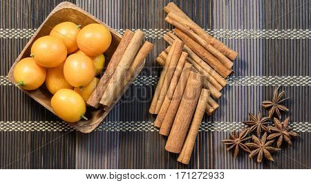 Fragrant cinnamon sticks and sweet kumquat in wooden bowl