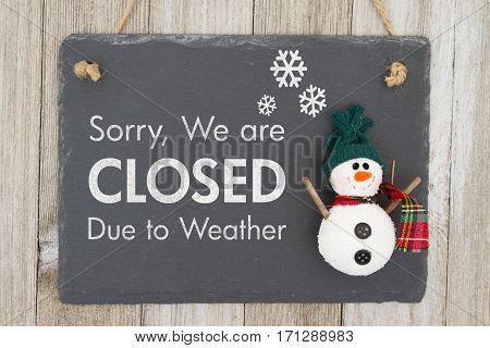 Closed due to weather sign A chalkboard sign with a snowman with text Closed due to weather on weathered wood