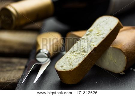 Chunk and thick cut off slice of smoked goat cheese with fork on black stone board bottle of wine in the background gourmet meal close up