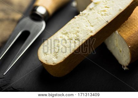Chunk of smoked goat cheese and a cut off thick slice with fork black stone board close up selective focus