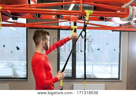 young sporty bearded man prepares for exersising in gym Adjust the length of the sling straps