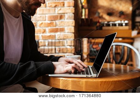 Cropped omage of Bearded man sitting by the table and using laptop in cafe