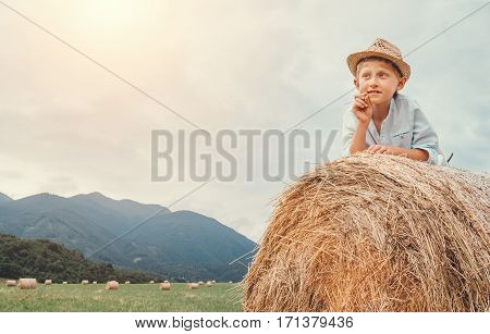 Boy in sraw hat lying on hay roll