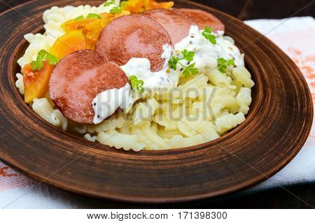 Galetti Pasta with pieces of sausage yellow tomatoes and creamy mustard sauce in a clay bowl on dark wooden background.