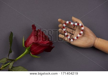 Wooden hand holding heart with red rose flower on gray background Love present card concept with copy space. Valentine's day theme