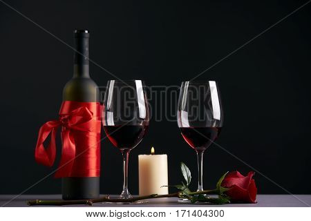 Wine bottle and two wineglasses with red rose and candle on a dark background. Valentine's day theme concept