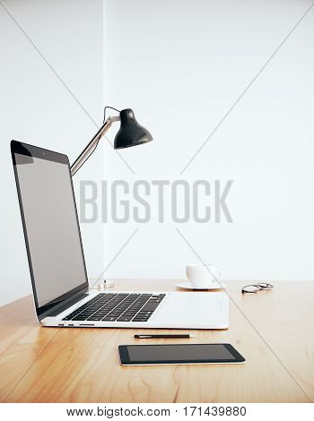 Side view of wooden desktop with blank laptop coffee cup tablet glasses and other items on concrete background. Mock up 3D Rendering