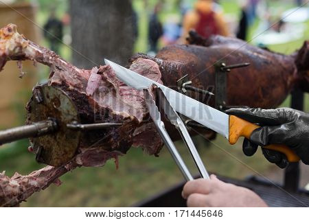 Barbecue picnic at country fair. Lamb roasted at spit. Grill, big piece of meat at rolling skewer. Street vendor, professional chef hands cooking bbq food, unrecognizable. Catering concept