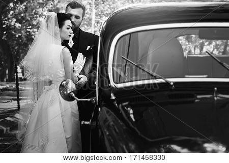 Luxury Elegant Wedding Couple Embracing At Stylish Black Car In Light. Gorgeous Bride And Handsome G
