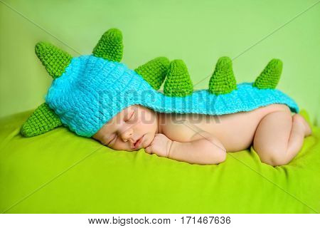 Cute newborn baby boy sleeping on green cover in dinosaur costume