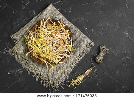 Bean sprouts in the wooden plate on sackcloth. Mungbean Sprouts in bundle tied vervevkoy. Dark black concrete background. Top view from above and copy space.