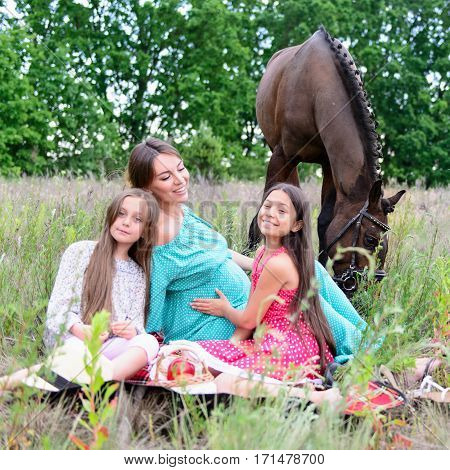 family young pregnant woman and children daughter with brown horse on the field