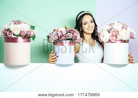 Sexy young pretty woman or cute smiling girl with crown on head has long hair in white dress with lilac rose and peony flowers bouquet boxes on green background