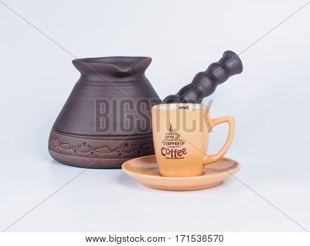 Picture of the beige-coloured coffee cup near dark brown jezve isolated on white background. Handmade earthenware. Side view.