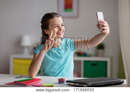 people, children and technology concept - girl with laptop computer and smartphone taking selfie or having video call at home