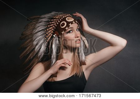 Portrait perfect woman in the garb of American Indians in the smoke on a gray background. Hat made of feathers. Mysterious mystical person a sexy body a beautiful face