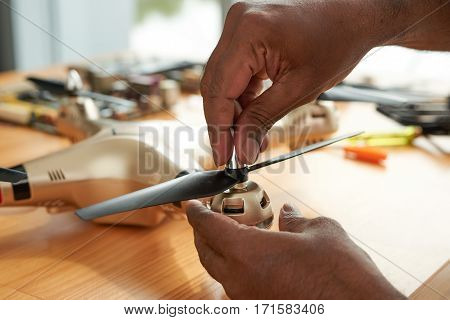 Close-up shot of male hands fixing propeller of drone with four rotors, wooden table with tools and spare parts observed on background