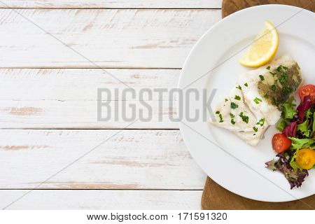 Fried cod fillet and salad in plate on white wooden background