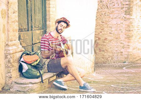 Traveler man playing guitar sitting in old italian town next at retro house - Young musician on summer journey street photography - Nostalgic concept with vintage filter effect and soft tones