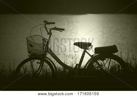 retro vintage bicycle near the lake at sunset moment. silhouette bicycle at the sunset with grass field.big mountain and sunset background.journey concept.lonely concept.filtered image