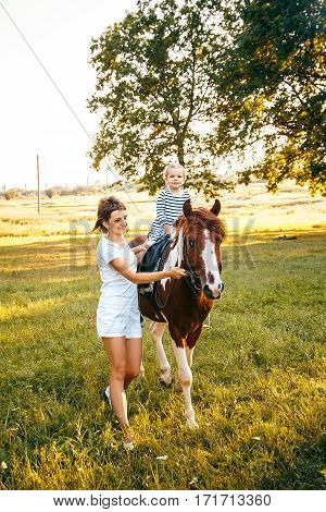 Little girl riding on a horseback with her mother walking nearby.