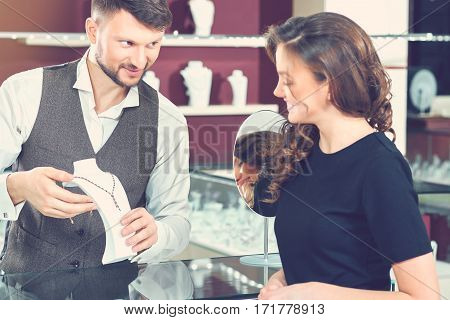 Professional advice. Beautiful young cheerful woman buying a necklace from a professional jeweler at the local boutique shopping shopaholic consumerism choosing buyer spending money femininity concept
