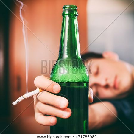 Toned Photo of Tired Young Man sleep with Bottle of the Beer and Cigarette