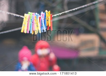 plastic varicoloured clothes pins on the rope in spring rainy day with water drops and two little girls unfocused