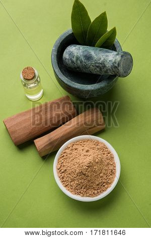Chandan or sandalwood powder with traditional mortar, sandalwood sticks, perfume or oil and green leaves. selective focus