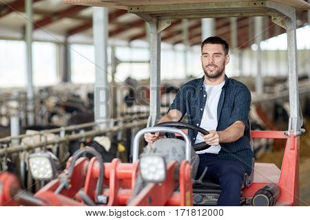 farming, agriculture and people concept - happy young man or farmer driving tractor at farm