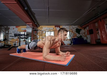 Confident muscled young man wearing sport wear and doing plank position while exercising on the floor at the gym. Plank it