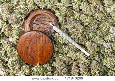 Wood grinder and spliff with dry cannabis buds background
