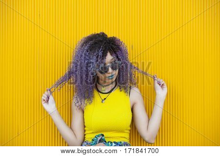 portrait of a teen woman with purple afro hair and colorful glasses  isolated on yellow background
