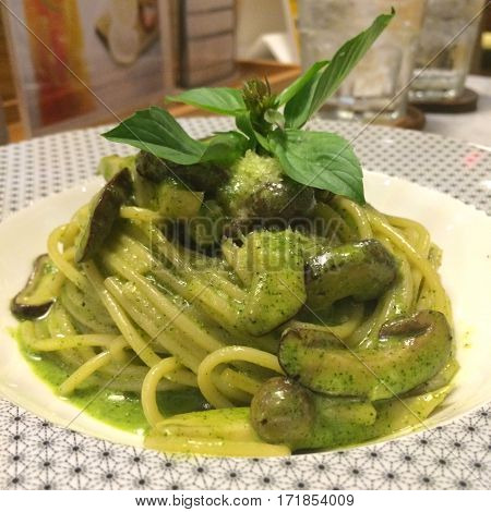 Stylist food Close up Italian pasta spaghetti homemade green pesto sauce mushroom top with basil leaf on white plate with blur restaurant background. healthy vegetarian food. Italian food concept.