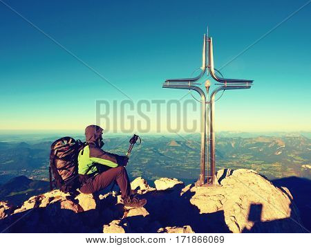 Tired Hiker Sit Bellow Crucifix On Mountain Peak. Iron Cross At Alps Mountain Top