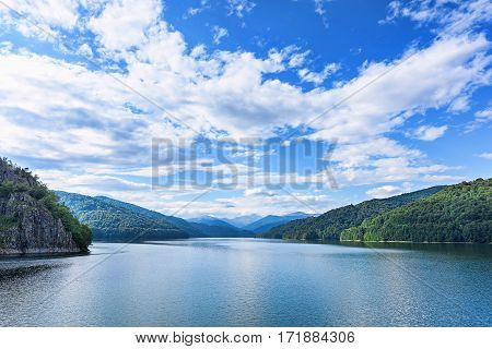 Photo of vidraru lake in fagaras, created on the dam in carpathian, blue sky and bog white clouds, chain of mountains, Romania