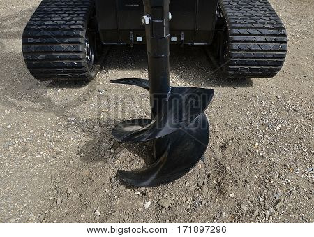 New auger for drilling holes into the ground mounted in front a tractor with rubber tracks.