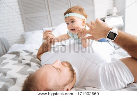 Happy with my daddy. Involved smiling cute toddler girl lying on her father in the bedroom and smiling while resting