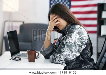 Pretty female soldier working with laptop while sitting at table in headquarters building