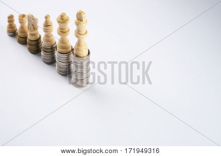 Growing coins stacks on white background. White chess figures standing on coins meaning power and career growth. Financial growth saving money business finance wealth and success concept.