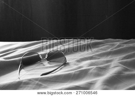 A Pair Of Aviator Glasses On Bed Sheets.