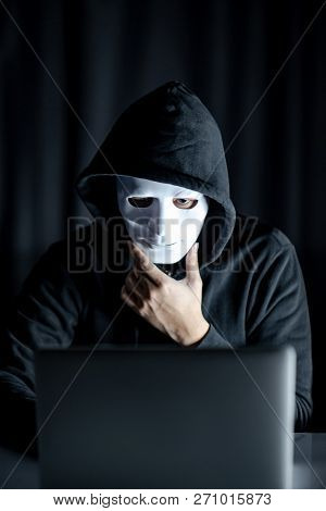 Mystery Male Hoodie Hacker Holding White Mask Looking At Laptop Computer. Anonymous Social Masking. 